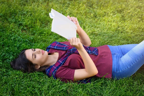 Ung Kvinna Läser Bok Medan Liggande Grönt Gräs Utomhus — Stockfoto
