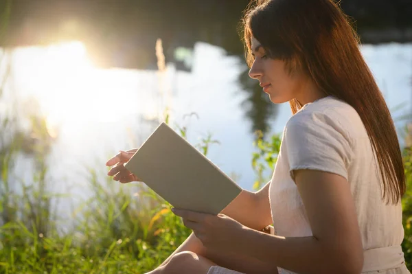 阳光明媚的日子 年轻女子在湖边看书 — 图库照片