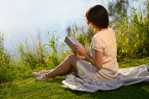 阳光明媚的日子 年轻女子在湖边看书 — 图库照片