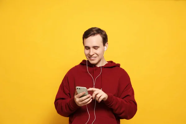 Przystojny Młody Człowiek Słuchawkami Smartfonem Żółtym Tle — Zdjęcie stockowe