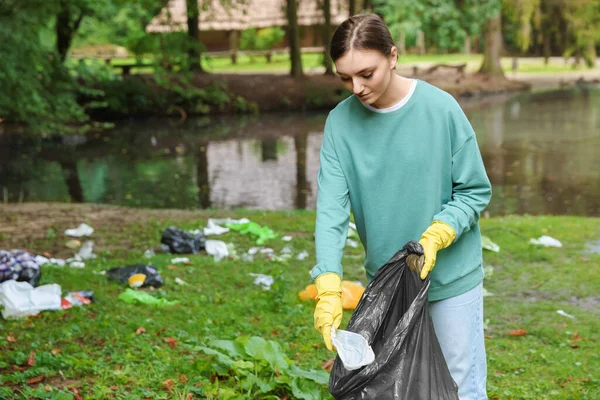 公園でゴミを集めるビニール袋を持つ若い女性 — ストック写真