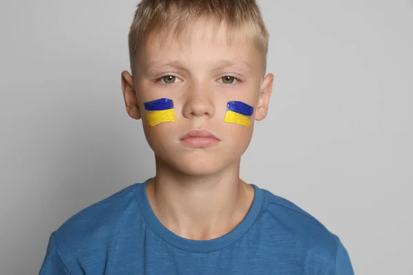 Little boy with drawing of Ukrainian flag on face against light grey background