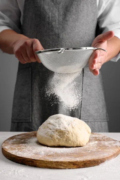 stock image Man sprinkling flour over dough at table near grey wall, closeup