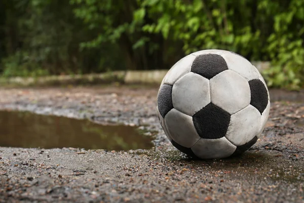 Dirty soccer ball near puddle on ground, space for text