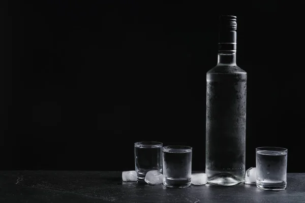 ウォッカのボトルと黒を背景にテーブルの上に氷とショットグラス テキストのスペース — ストック写真