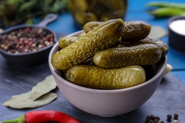 Bir kase salatalık turşusu ve yemek malzemesi mavi ahşap masada, yakın plan.