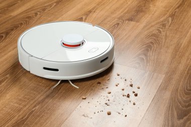 Robotik elektrik süpürgesi ahşap zemindeki toprağı kaldırıyor.
