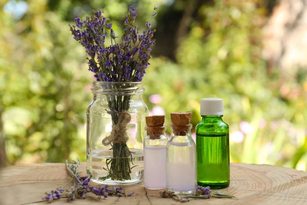 Beautiful lavender flowers and bottles of essential oil on wooden stump
