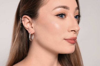 Beyaz arka planda kulak ve dudak piercingli genç bir kadın, yakın plan.