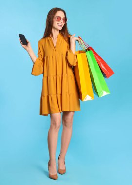 Alışveriş torbaları ve açık mavi arka planda akıllı telefonları olan mutlu genç bir kadın. Büyük indirim.