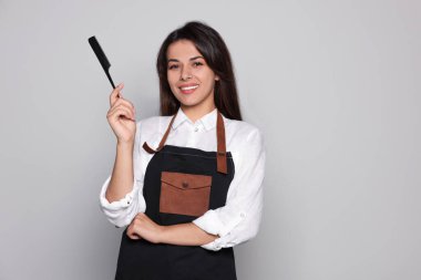 Açık gri arka planda profesyonel taraklı mutlu bir kuaför portresi. Metin için boşluk