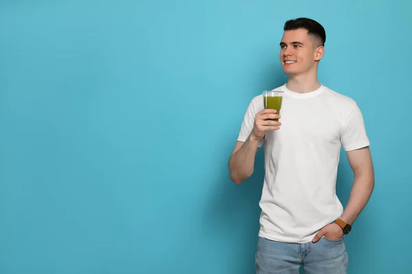 Handsome young man with glass of juice on light blue background, space for text