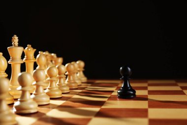 Siyah piyon, tahtadaki beyaz parçaların önünde, siyah arka plana karşı. Rekabet konsepti