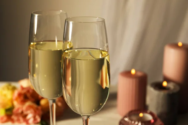 Glasses of sparkling wine, flowers and burning candles on white table, closeup