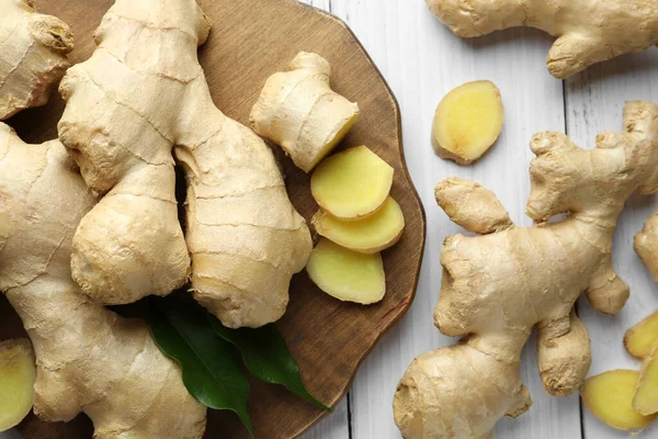 Cut and whole fresh ginger with leaves on white wooden table, flat lay