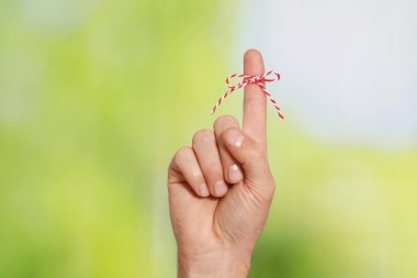 Yeşil bulanık arkaplanda hatırlatma olarak bağlı yay ile işaret parmağı gösteren adam, yakın plan