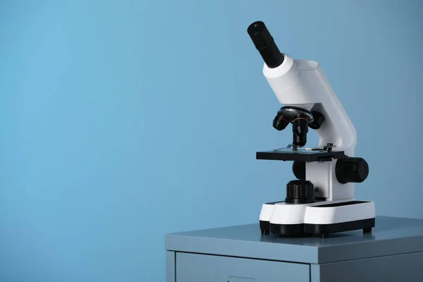 Modern microscope on table against blue background. Space for text