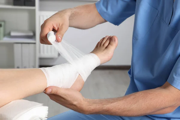 Doctor applying bandage onto patient's foot in hospital, closeup