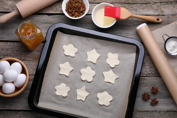 Parchment paper, baking pan with raw cookies and different ingredients on wooden table, flat lay