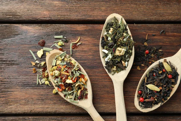 Spoons with dried herbal tea leaves on wooden table, flat lay