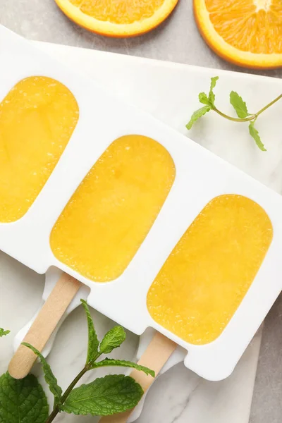 Tasty orange ice pops in mold on light grey table, flat lay. Fruit popsicle