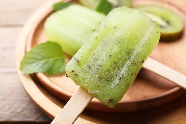 Plate of tasty kiwi ice pops on wooden table, closeup. Fruit popsicle