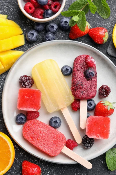 Plate of different tasty ice pops on black textured table, flat lay. Fruit popsicle