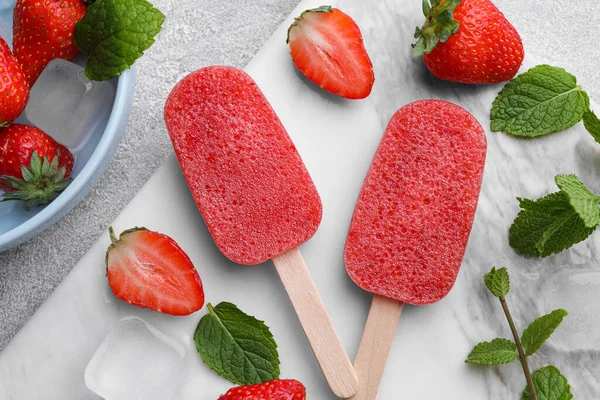Tasty strawberry ice pops on grey table, flat lay. Fruit popsicle