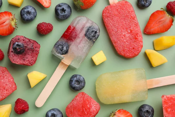 Different tasty ice pops on pale green background, flat lay. Fruit popsicle