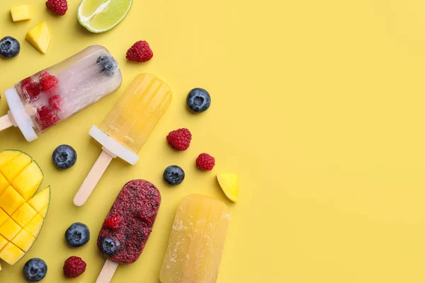 Different fruit ice pops on light yellow background, flat lay. Space for text