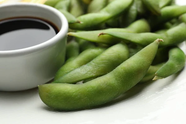 Green edamame beans in pods served with soy sauce on plate, closeup