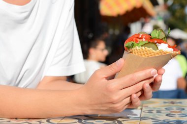 Dışarıdaki renkli fayanslı masada falafel ve sebzeli gofret tutan kadın, yakın plan. Sokak yemeği.