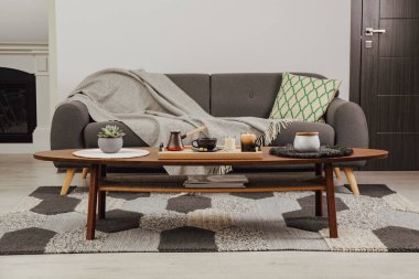 Taze demlenmiş kahve ve dekoratif öğeler oturma odasındaki kanepenin yanındaki ahşap masada.