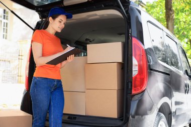 Dışarıdaki paketlerin ve teslimat kamyonlarının yanında kurye yazısı var.