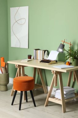 Writer's workplace with typewriter on wooden desk near pale green wall in room