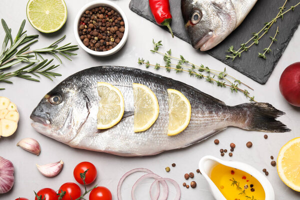 Плоская композиция из свежей сырой рыбы дорадо и ингредиентов на светло-сером столе