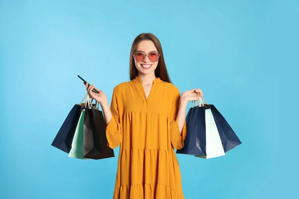 Glückliche Junge Frau Mit Einkaufstaschen Und Smartphone Auf Hellblauem Hintergrund — Stockfoto