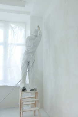 Dekoratör, pencerelerin yakınındaki merdivene duvar boyuyor.