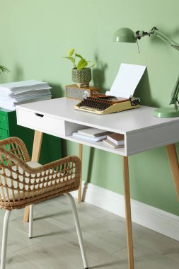 Writer's workplace with typewriter on wooden desk near pale green wall in room
