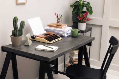 Typewriter and stack of papers on dark table in room. Writer's workplace