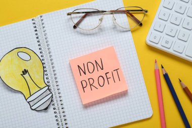 Sarı zemin üzerinde Kâr amacı gütmeyen, defter, gözlük, kalem ve kağıt ampul olmayan kağıt bir not.