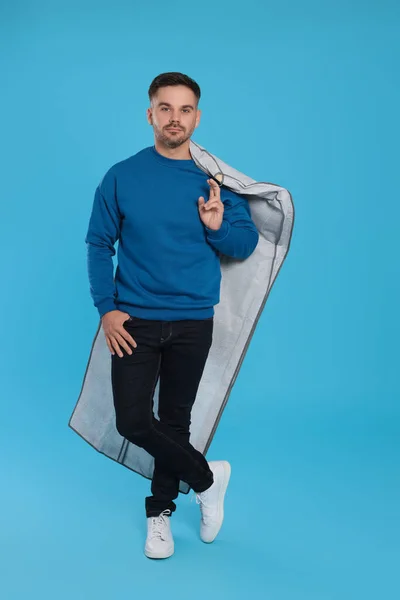 Man holding garment cover with clothes on light blue background. Dry-cleaning service