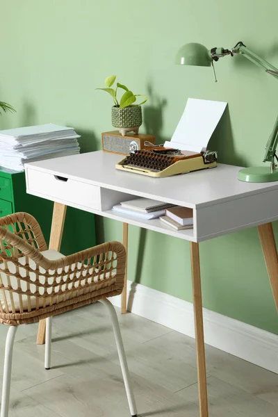 Writer\'s workplace with typewriter on wooden desk near pale green wall in room