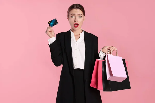 Überraschte Junge Frau Mit Einkaufstaschen Und Kreditkarte Auf Hellrosa Hintergrund — Stockfoto