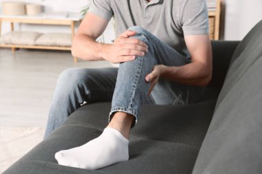 Evdeki kanepede bacağında ağrıdan muzdarip bir adam, yakın plan.