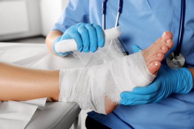 Doctor applying bandage onto patient's foot in hospital, closeup