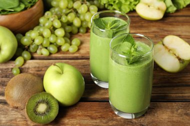 Bardakta yeşil smoothie ve ahşap masada taze malzemeler.