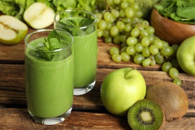 Bardakta yeşil smoothie ve ahşap masada taze malzemeler.
