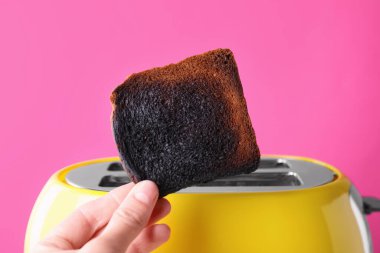 Ekmek kızartma makinesinin yanında pembe arka planda yanmış bir kadın, yakın plan.