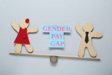 Cinsiyet farkı. Minyatür bir kadın ve erkeğin tahta figürleri açık gri arka plana karşı tahterevalli gibi.